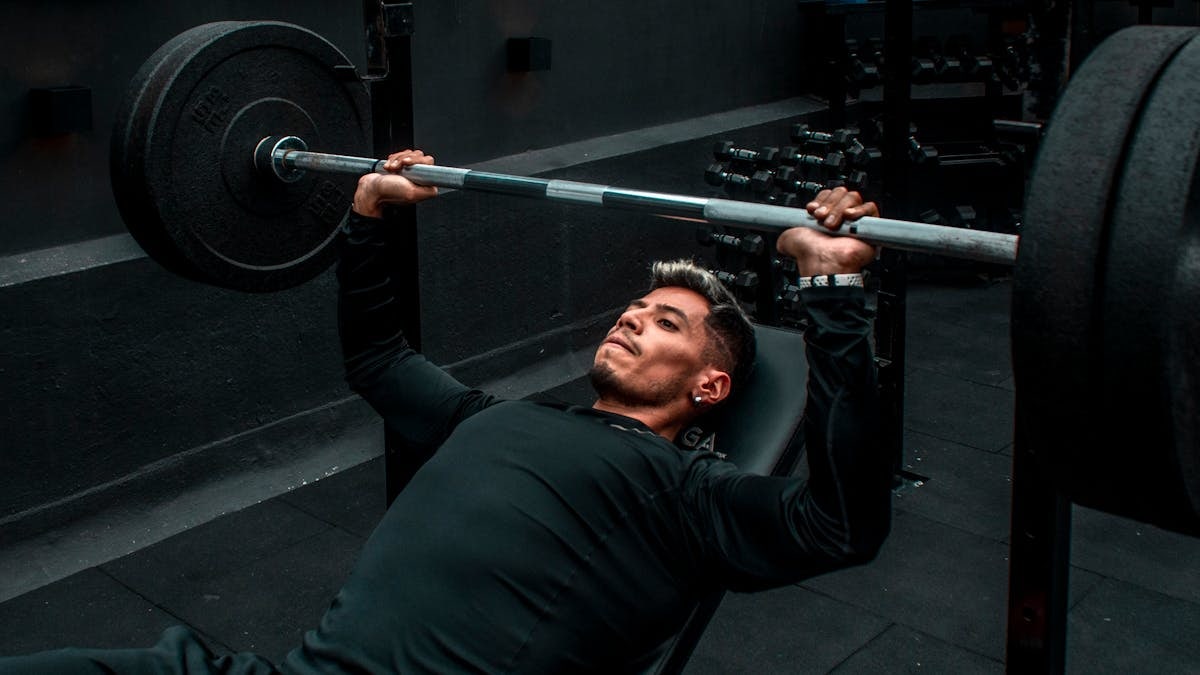 Man performing bench press with heavy barbell in a gym setting, focusing on strength training.